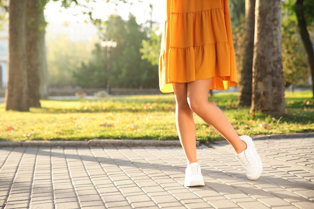 Woman wearing stylish yellow dress and sneakers in park, closeup